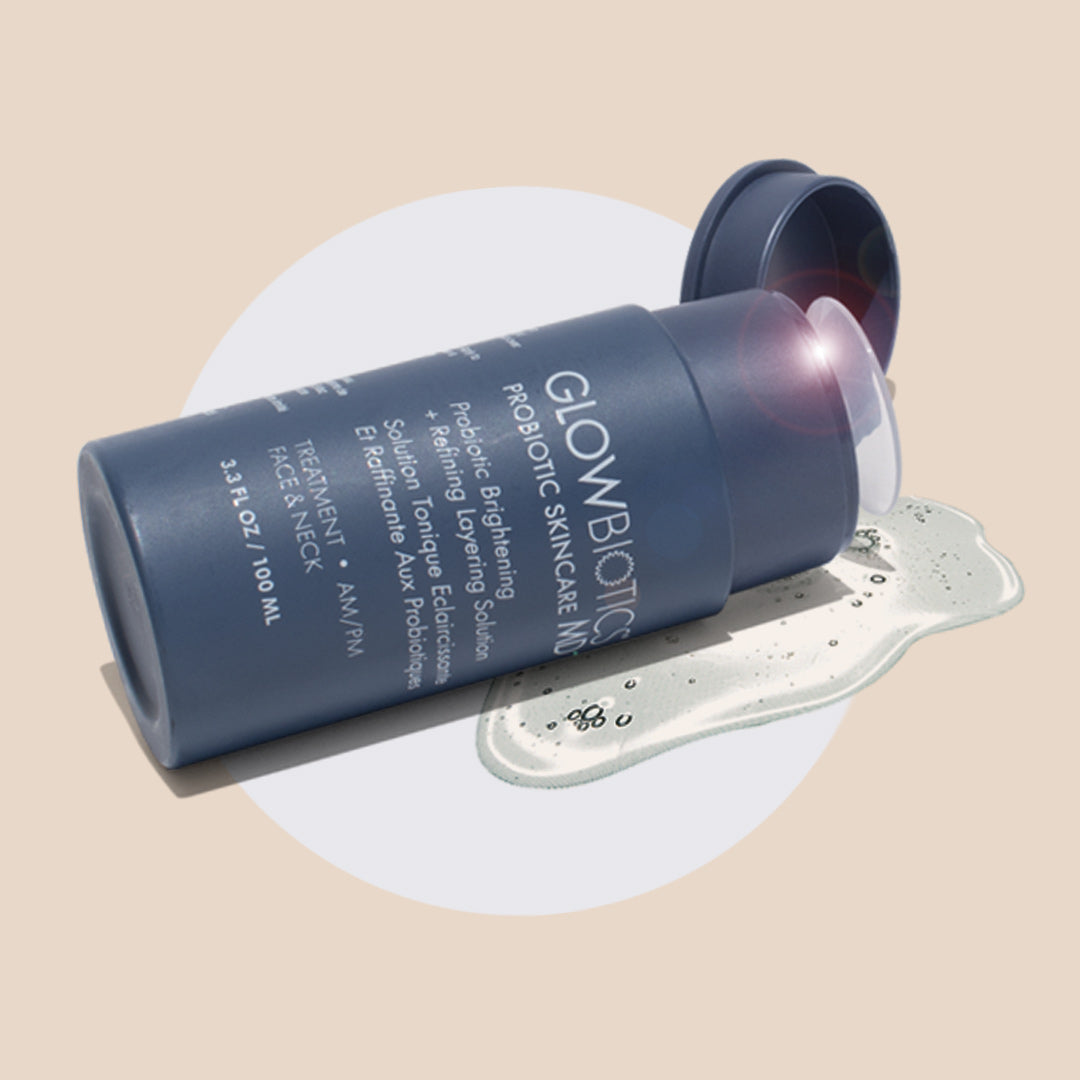 Glowbiotics Probiotic Brightening + Refining Layering Solution bottle lying on a beige background with clear liquid product spilled next to it