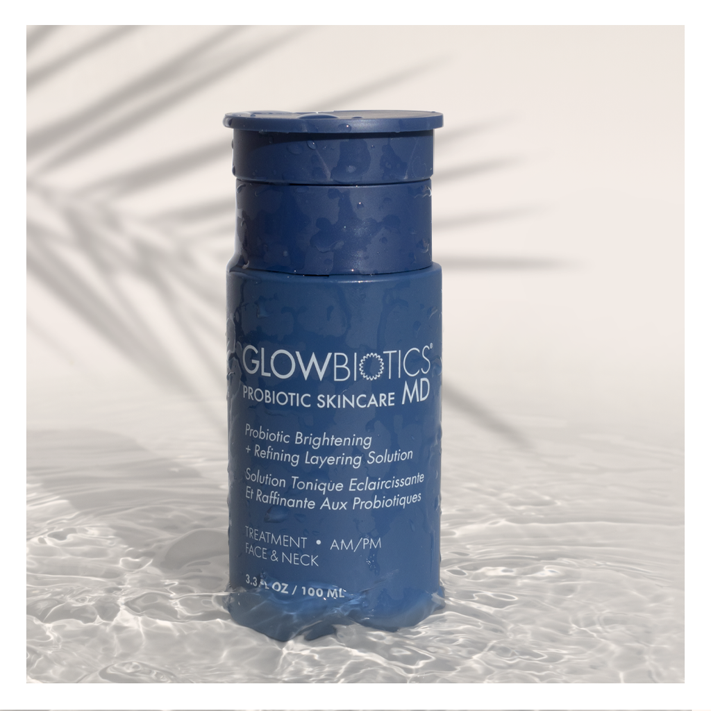 Glowbiotics Probiotic Brightening + Refining Layering Solution bottle standing upright on a textured white surface with palm leaf shadow