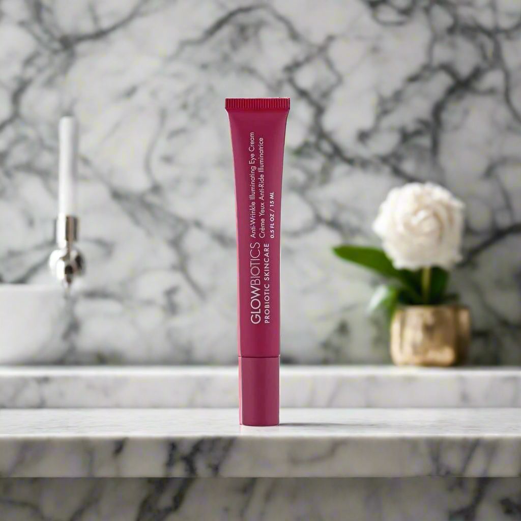 Tube of Glowbiotics Anti-Wrinkle Illuminating Eye Cream standing upright on a marble counter with a white rose in the background
