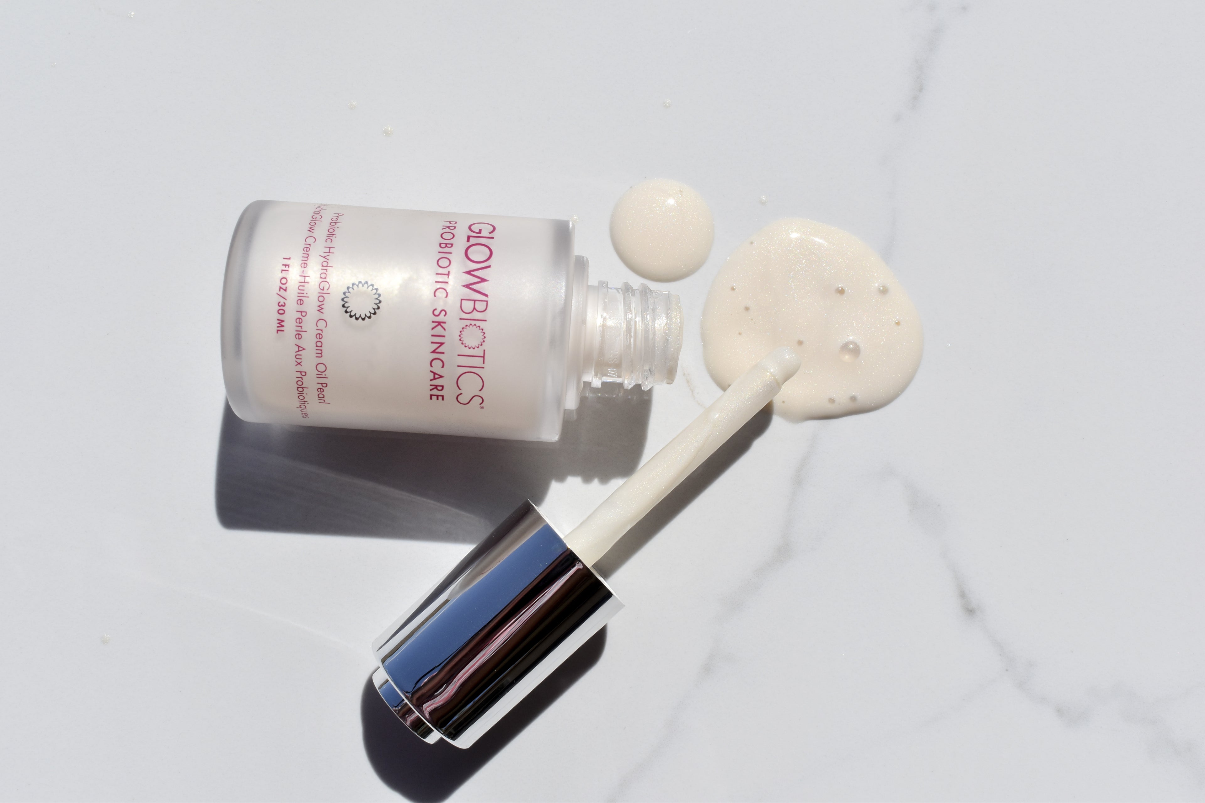 Cream-Oil Pearl bottle with formula dollops and dropper on white-marble background.