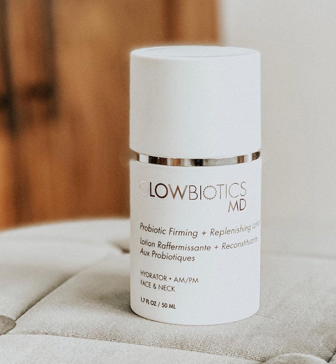 Lifestyle image of Glowbiotics Probiotic Firming + Replenishing Lotion on a beige cushioned surface
