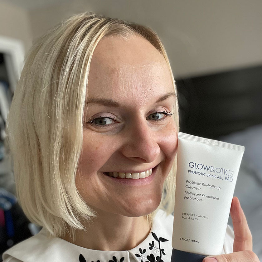 Woman indoors holding a Glowbiotics Probiotic Revitalizing Cleanser tube close to camera.
