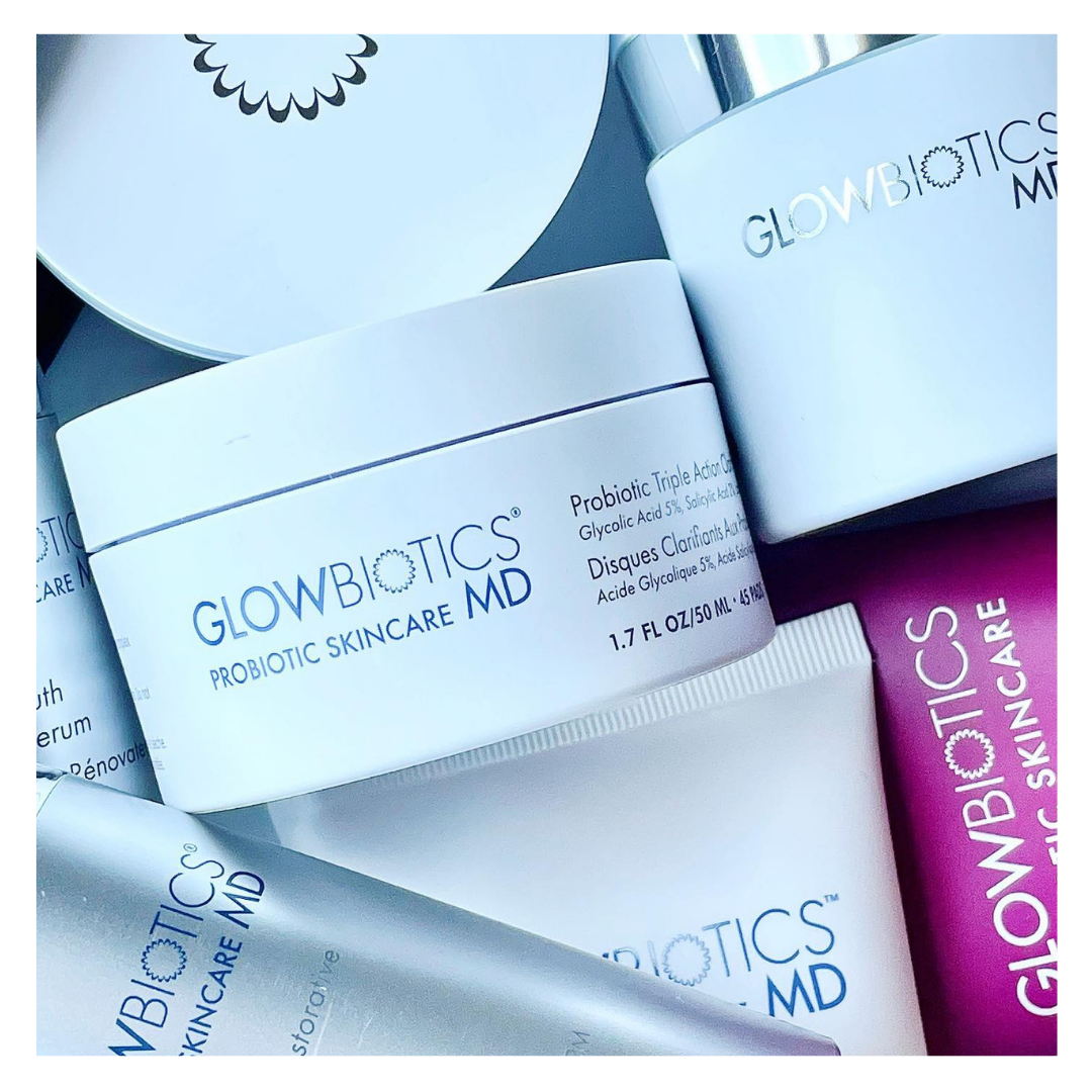Glowbiotics MD flat-lay: Probiotic Triple Action Clarifying Pads jar with cleansers and serums on a cool blue background.
