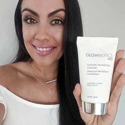 Woman holding Glowbiotics Revitalizing Cleanser tube against neutral background