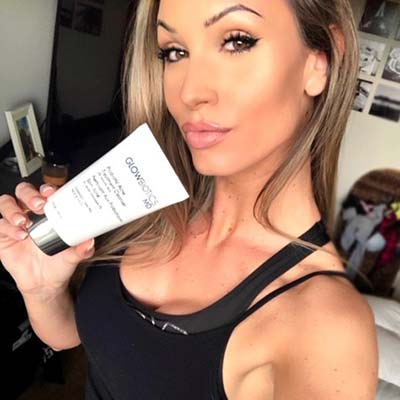 Woman posing indoors with Glowbiotics Revitalizing Cleanser tube