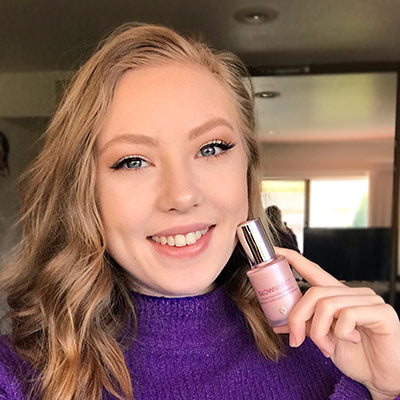 Woman in purple sweater holding Glowbiotics Illuminating Serum bottle.