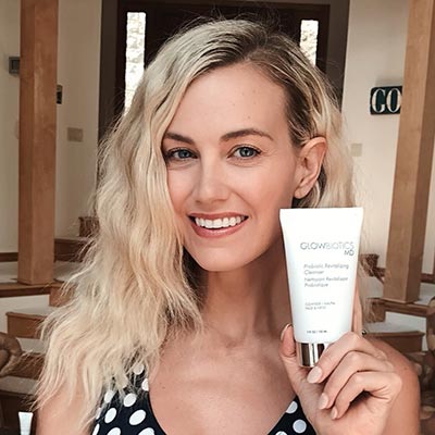Woman with wavy blonde hair displaying a Glowbiotics Tinted Sunscreen SPF 30 tube.
