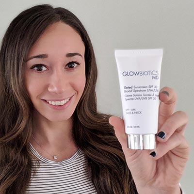 Woman presenting Glowbiotics Revitalizing Cleanser tube against neutral background.
