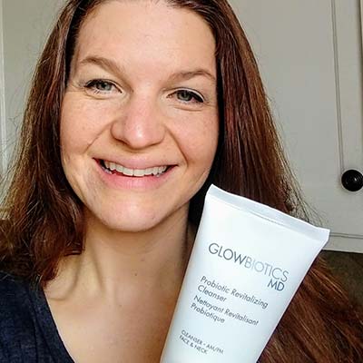 Smiling woman holding a Glowbiotics Tinted Sunscreen SPF 30 tube close to camera.