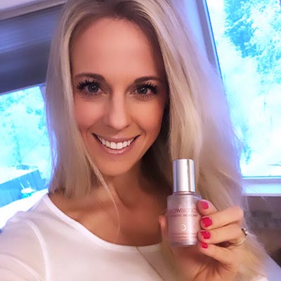 Smiling woman near window displaying Glowbiotics Illuminating Serum bottle.