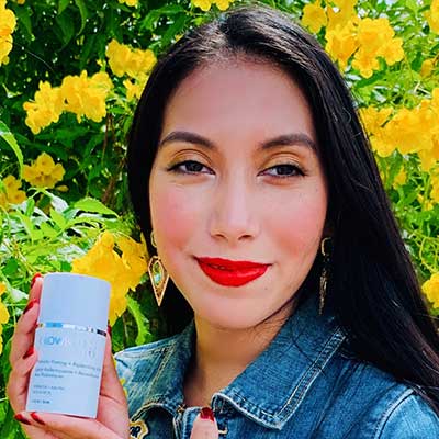 Woman outdoors with yellow flowers displaying a Glowbiotics Gentle Probiotic Calming Lotion.