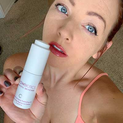 Woman in sleeveless top presenting a Glowbiotics Advanced Retinol Renewal Serum bottle.