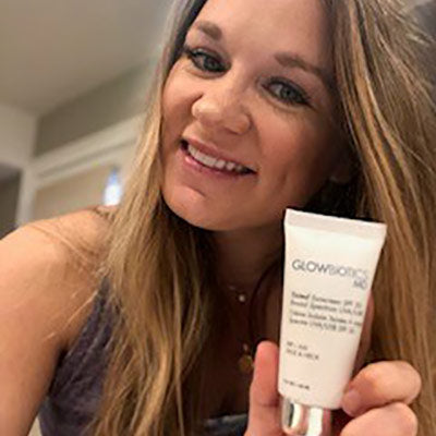 Woman indoors showing a Glowbiotics Tinted Sunscreen SPF 30 tube.