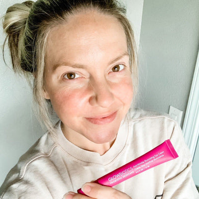 Woman in casual sweatshirt holding pink Glowbiotics eye-treatment tube.