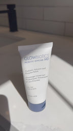 Tube of Glowbiotics Probiotic Volcanic and Enzyme Polish standing on a white surface with water running in the background