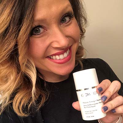 Woman holding a Glowbiotics Gentle Probiotic Calming Lotion jar while smiling.