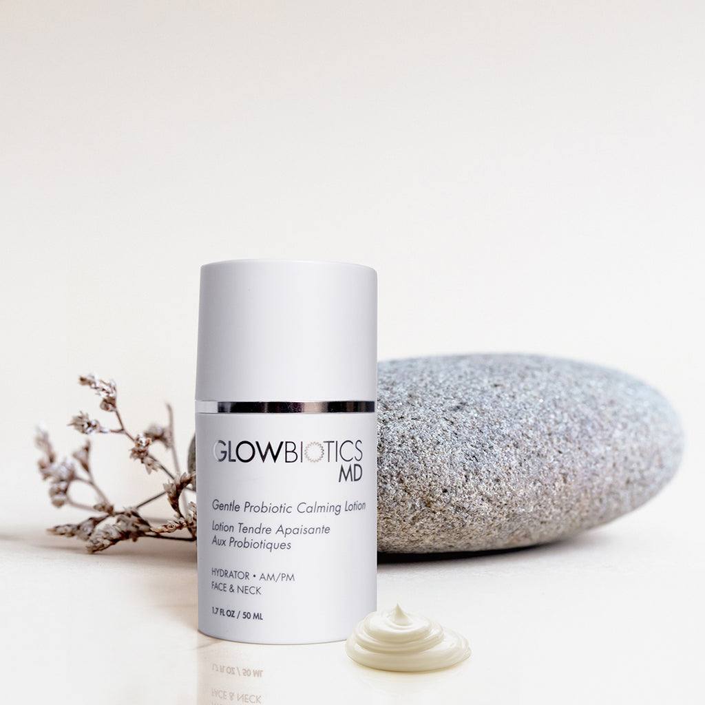 Glowbiotics Gentle Probiotic Calming Lotion bottle beside smooth stone and small dried plant on neutral background