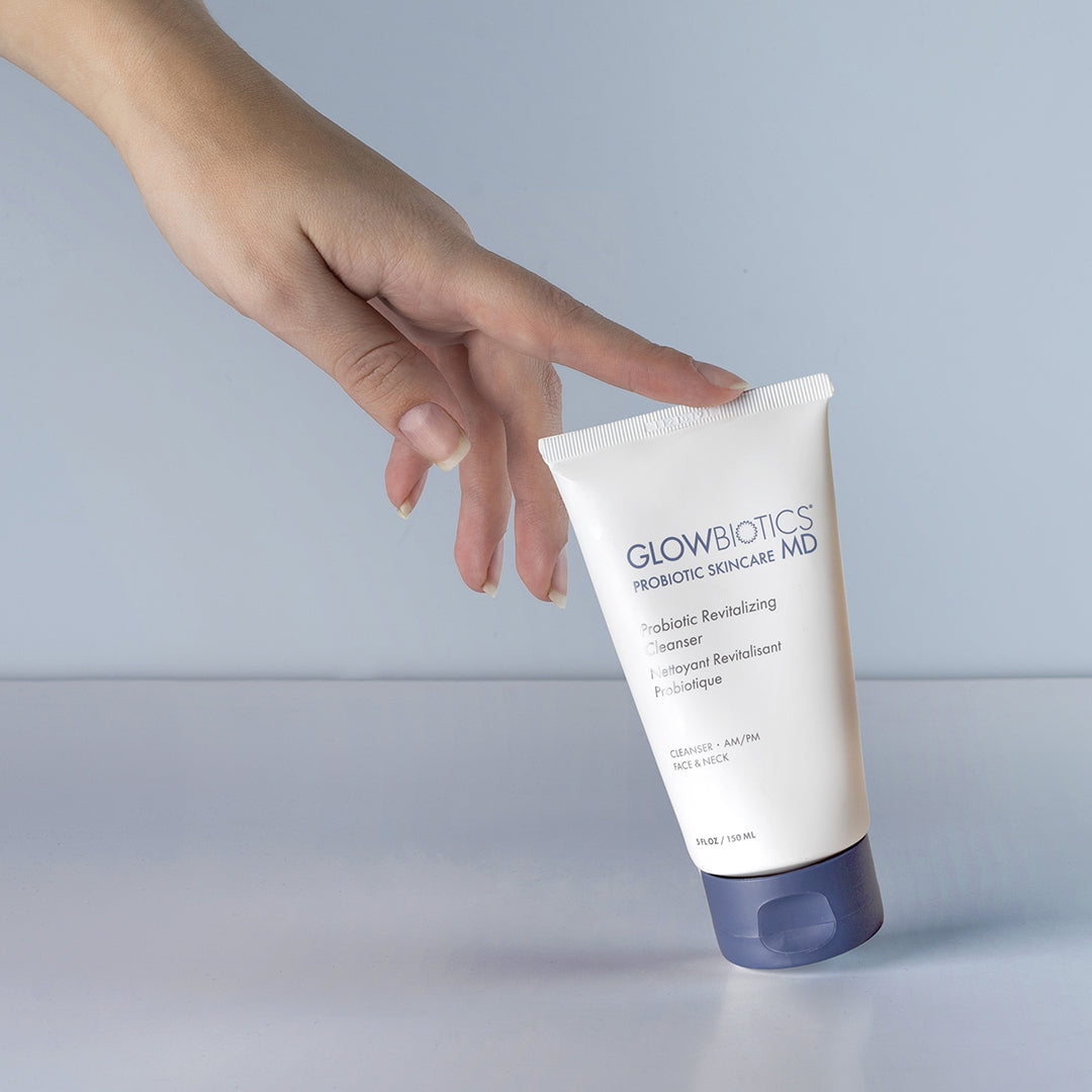 Hand holding Glowbiotics Probiotic Revitalizing Cleanser against blue background
