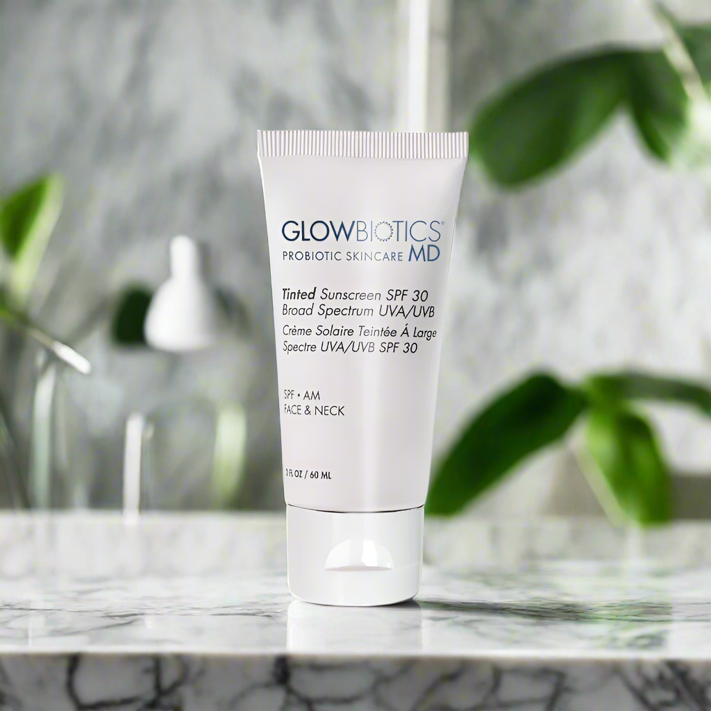 Glowbiotics Tinted Sunscreen SPF 30 Broad Spectrum UVA/UVB tube placed on a marble surface with green leaves blurred in the background for a lifestyle product shot
