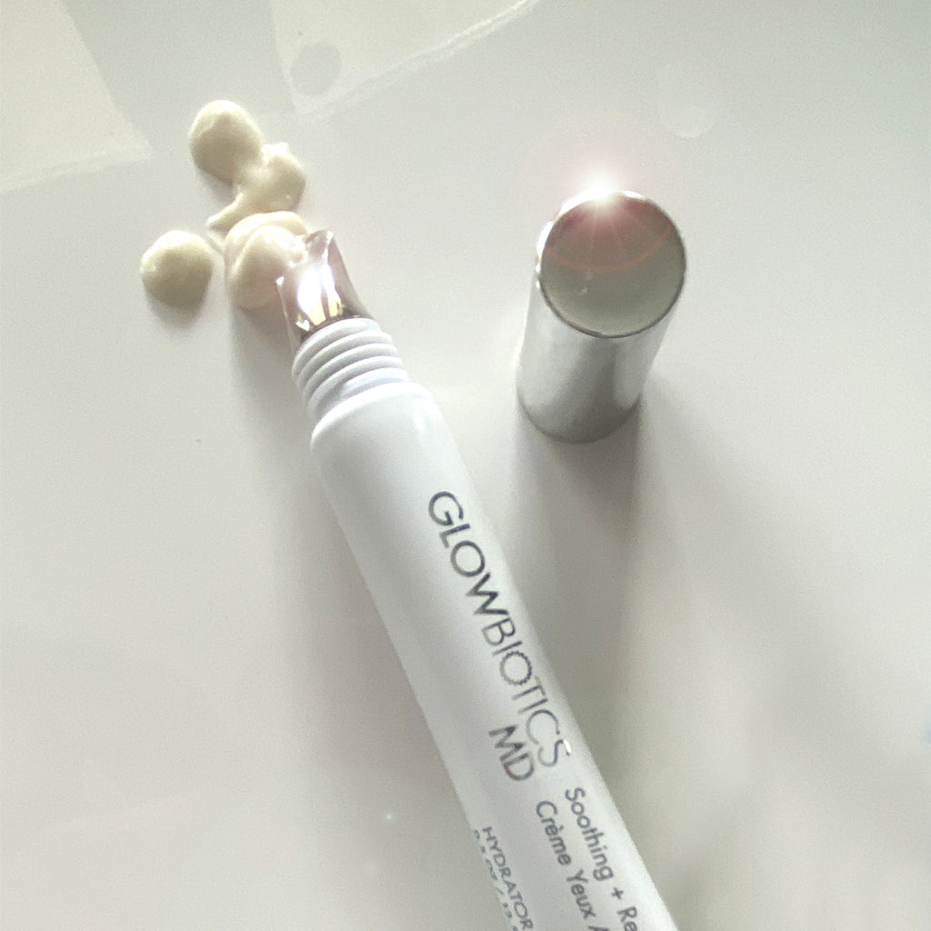 Glowbiotics Soothing + Revitalizing Eye Cream with cooling applicator tip, cap off, and cream swatches on white background