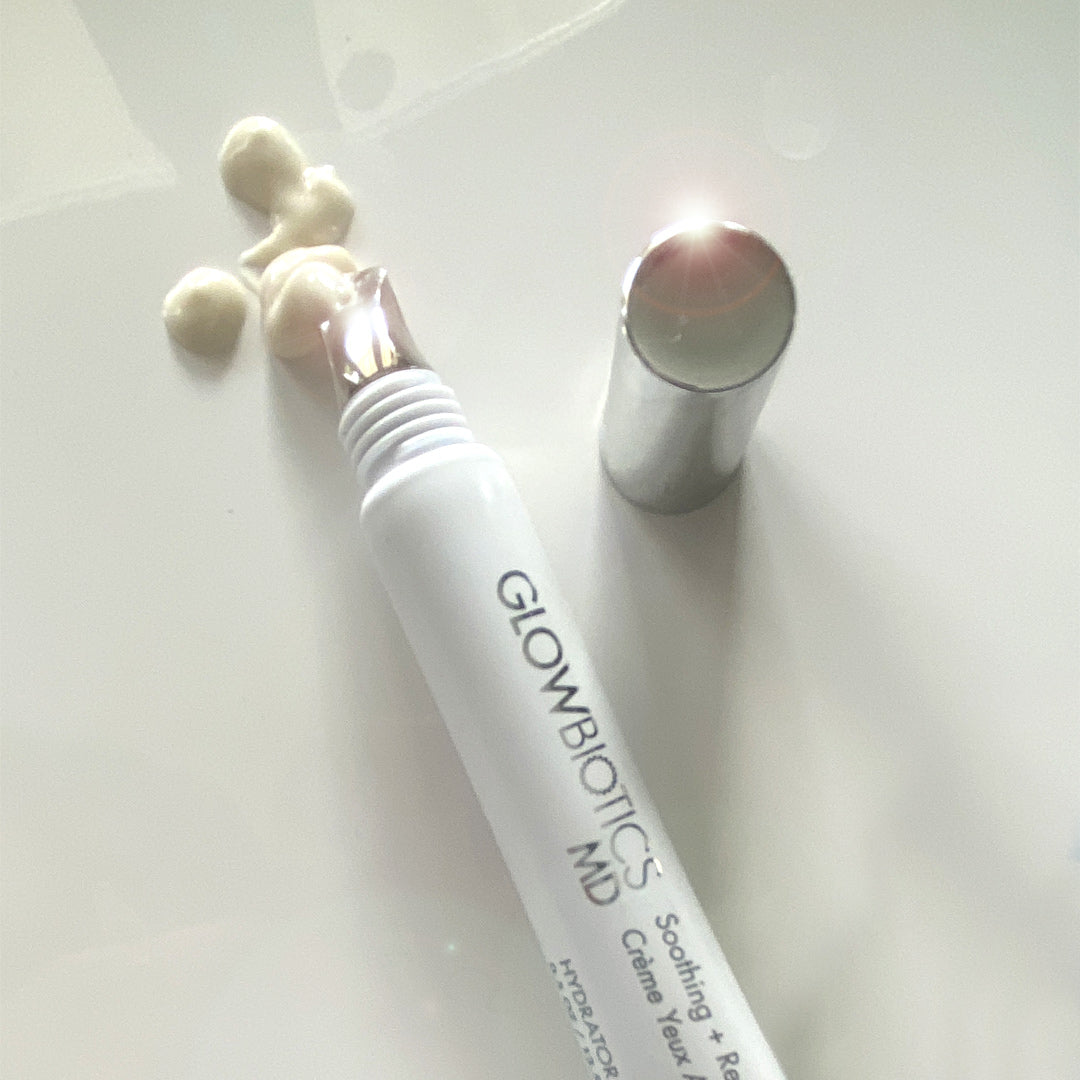 Glowbiotics Soothing + Revitalizing Eye Cream with cooling applicator tip, cap off, and cream swatches on white background