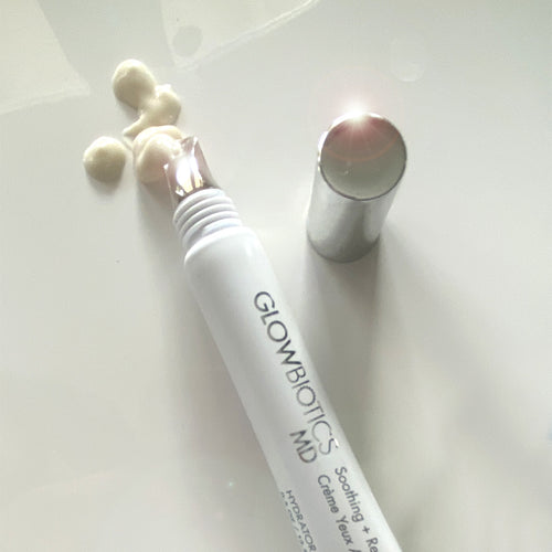 Glowbiotics Soothing + Revitalizing Eye Cream with cooling applicator tip, cap off, and cream swatches on white background